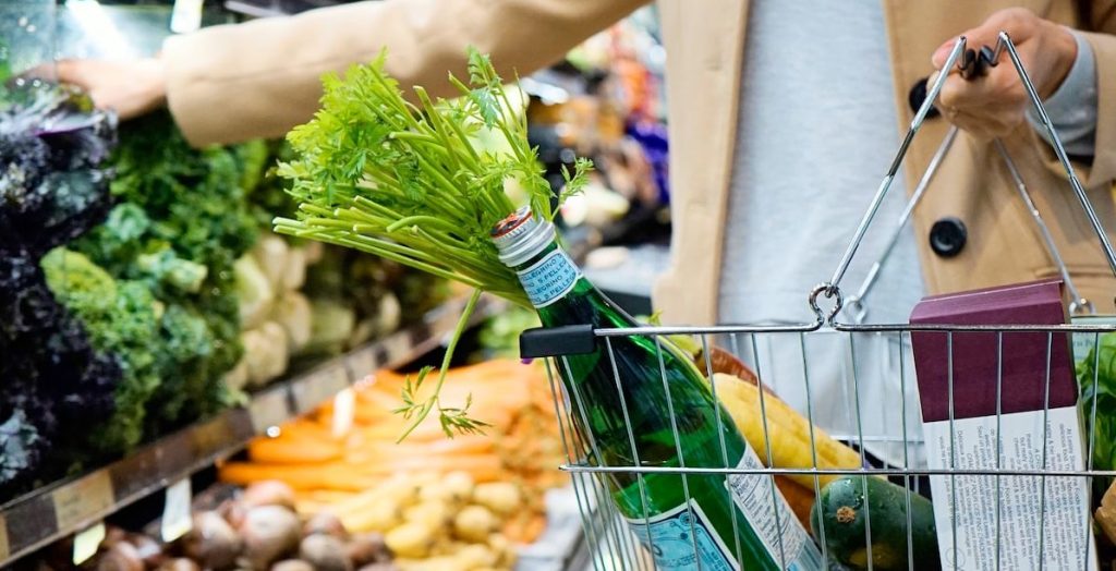 woman in white coat holding green shopping cart